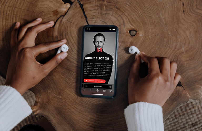 EliotXII website on a phone screen and hands holding airpods
